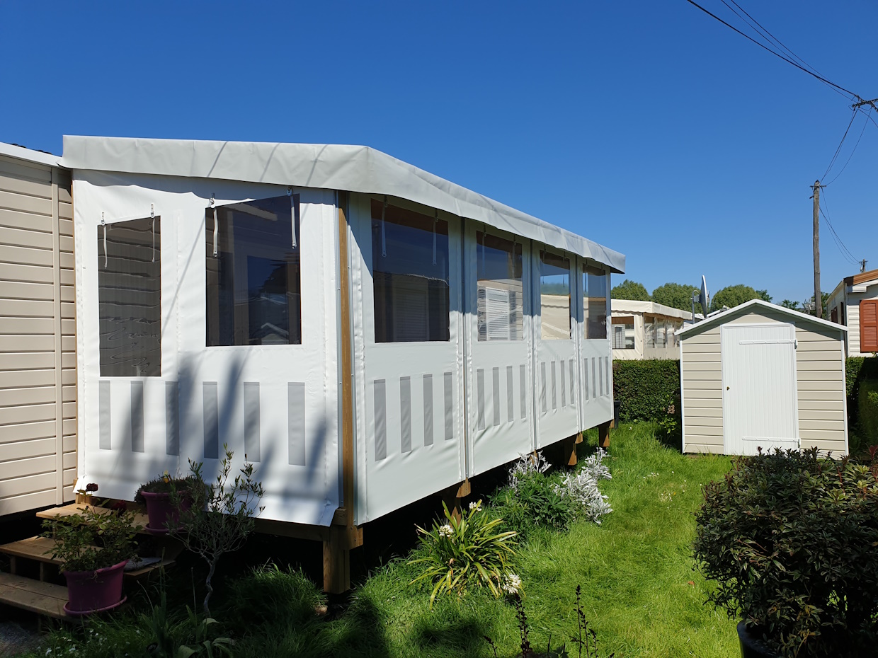 Mobil-home avec extension et abri dans jardin ensoleillé.